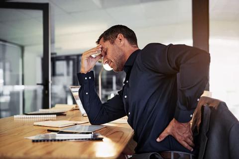 Man holding painful back at his desk